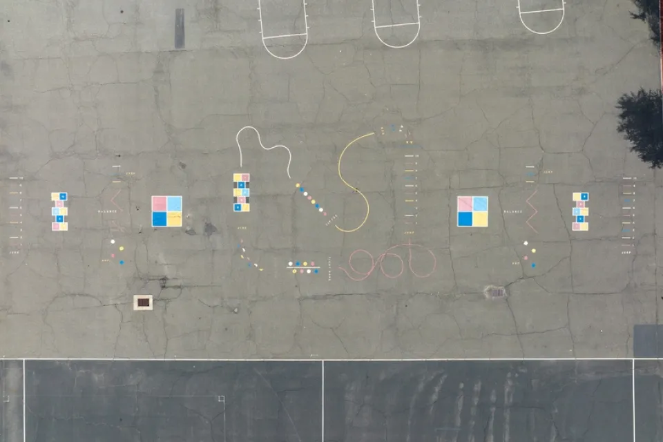 A school blacktop is viewed from bird’s eye view. The blacktop is adorned with painting and colors for games. but no children are present.